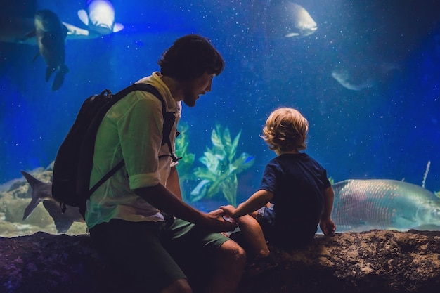 Father and son look at the fish in the aquarium in oceanarium
