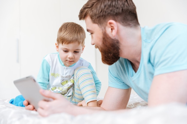 父と息子が横になって、家でタブレットで遊んでいます