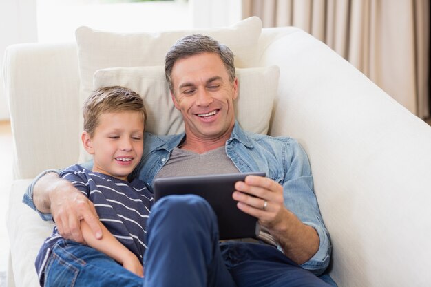 아버지와 아들이 소파에 누워 거실에서 디지털 태블릿을 사용하여