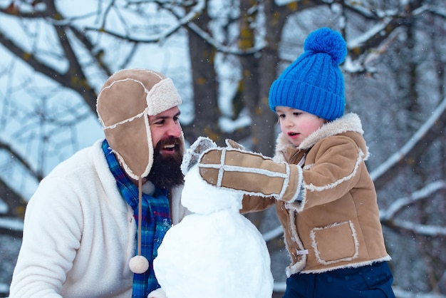 Father and son making snowman in the snow. Handmade funny snowman. Christmas holidays and winter new