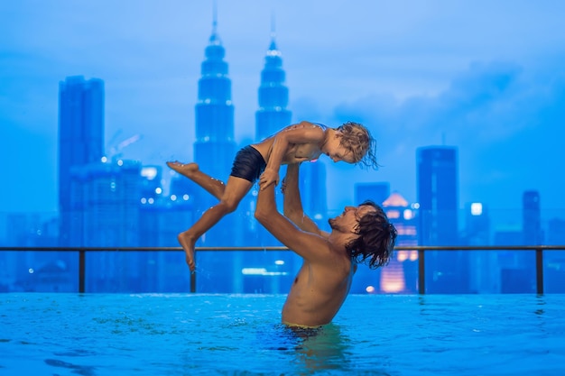 Father and son in outdoor swimming pool with city view in blue sky