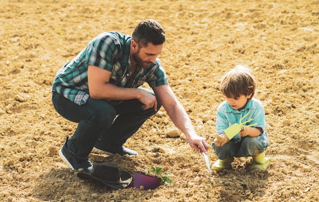 Father and son planting growing plants spring garden dad teaching little son care plants dig and shovel