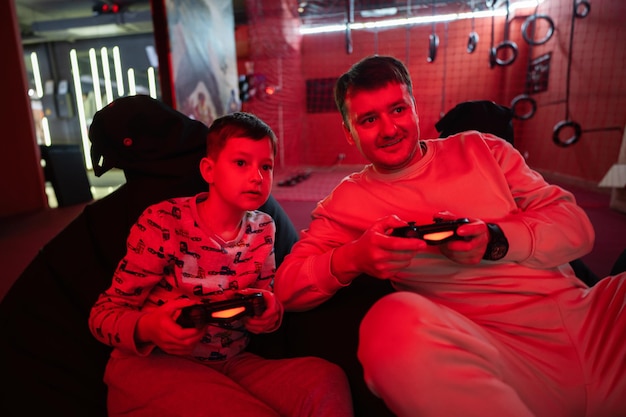 Father and son play gamepad video game console in red gaming room Dad and kid gamers