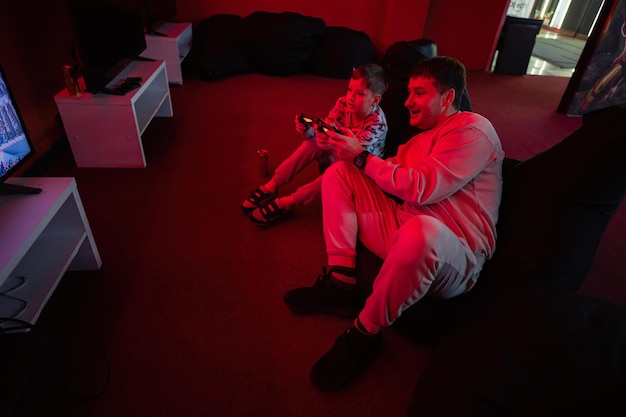 Father and son play gamepad video game console in red gaming room Dad and kid gamers