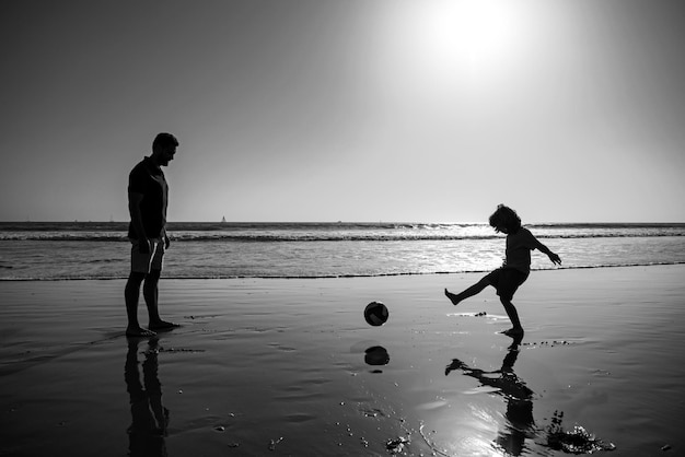 Father and son play soccer or football on the beach daddy with kid boy playing on a summer day