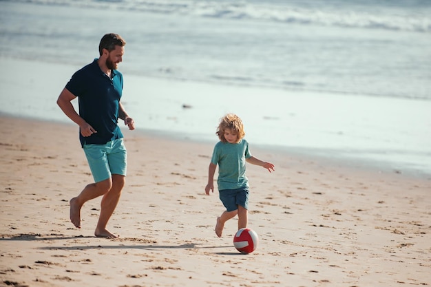 Father and son play soccer or football on the beach on summer family holidays dad and child enjoying