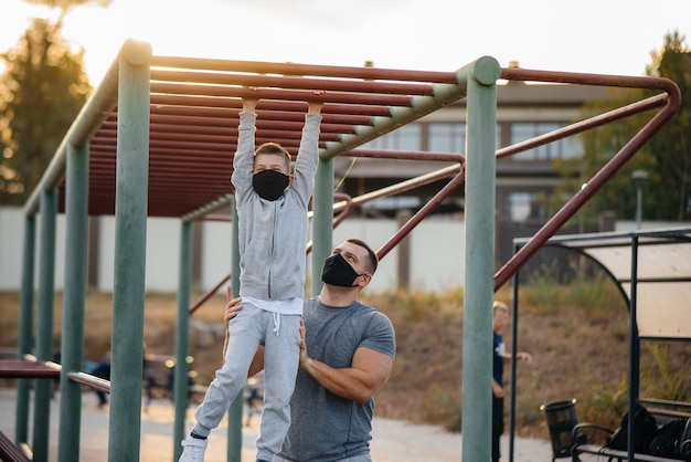 Отец и сын занимаются спортом на спортивной площадке в масках во время заката. Здоровое воспитание и здоровый образ жизни.