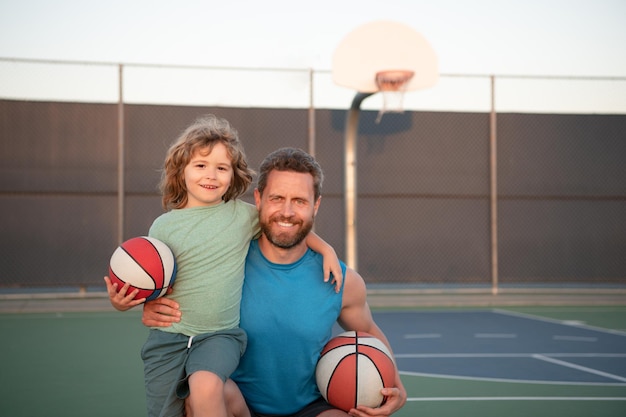 バスケットボールをしている父と息子遊び場でバスケットボールのボールを持っている小さな男の子を抱きしめるお父さんの肖像画