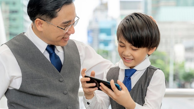 Father and son playing smart phone together on business district urban Dad and Son happy Asian family concept