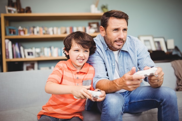 Father and son playing video game while sitting on sofa