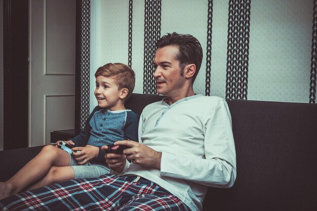 Father and son playing video games while sitting on sofa