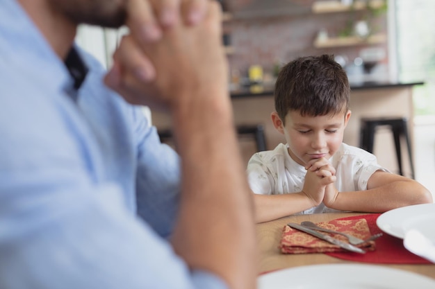 father and son praying before having lunch at dining table