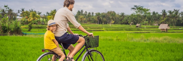 Padre e figlio vanno in bicicletta su un campo di riso a ubud bali viaggiano a bali con un banner per bambini