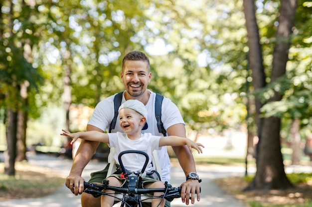 Father and son ride bicycle. Toddlers sit in a basket of bikes and wander around. Summer sunny family day, family bonding time. Active family weekend, vacation in the park with the family