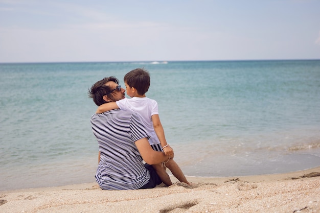 Father and son sit on the beach with sand in summer while on vacation