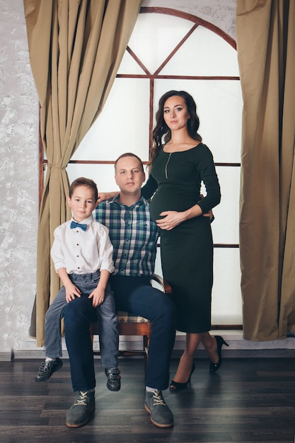 Father and son sitting on a chair with pregnant mother