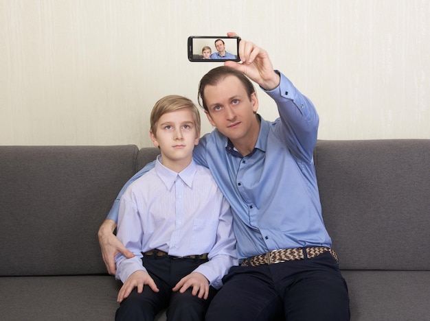 Father and son sitting on the couch and taking selfie photo together