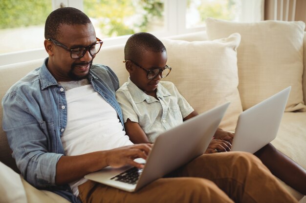 Father and son sitting on sofa and using laptop