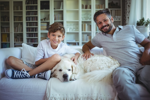 Father and son sitting on sofa with pet dog in living room