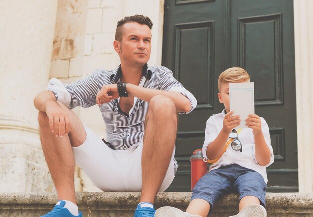 Photo father and son sitting on staircase in the city while visiting old town on summer vacation