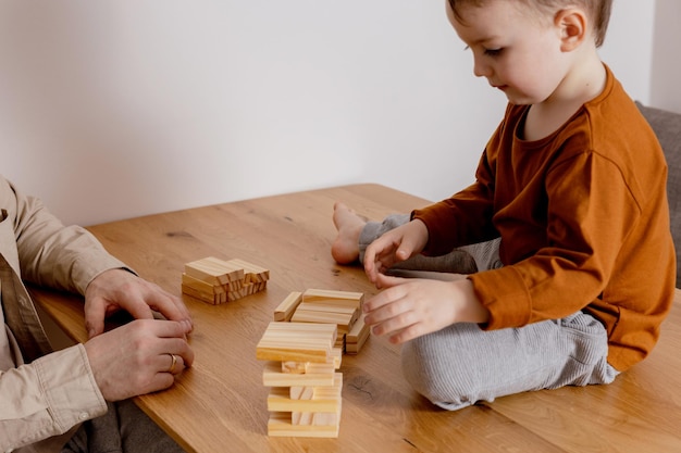 Father and son sitting together at home and playing with wooden blocks Jenga game Little boy and his father spending time together Family time Leisure activity indoors