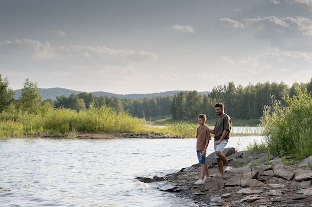 Father and son standing by lake while spending summer vacation in the country