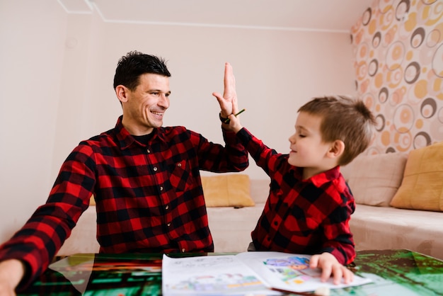 Photo father and son time. young father and cute sitting by the table with his cute son and drawing. high five.