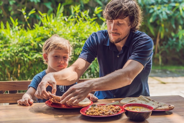 Father and son try Indian food in a cafe on the street