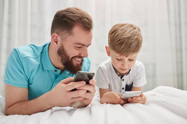 Father and son using gadgets in bedroom