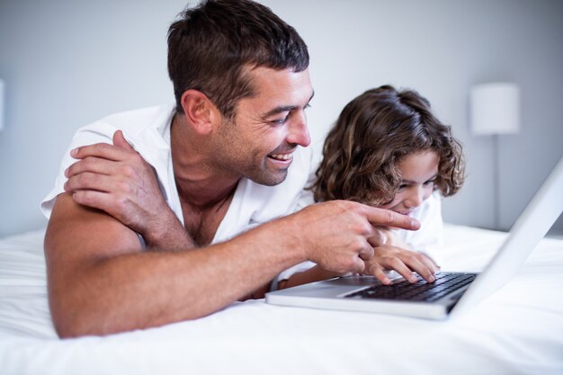 Father and son using laptop on bed