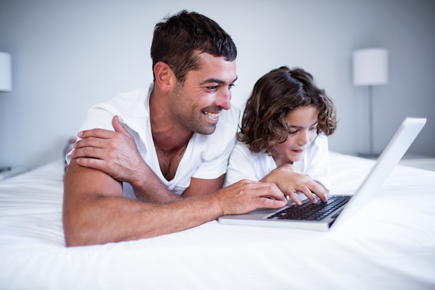 Father and son using laptop on bed