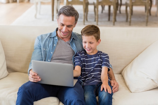 Father and son using laptop on sofa in living room