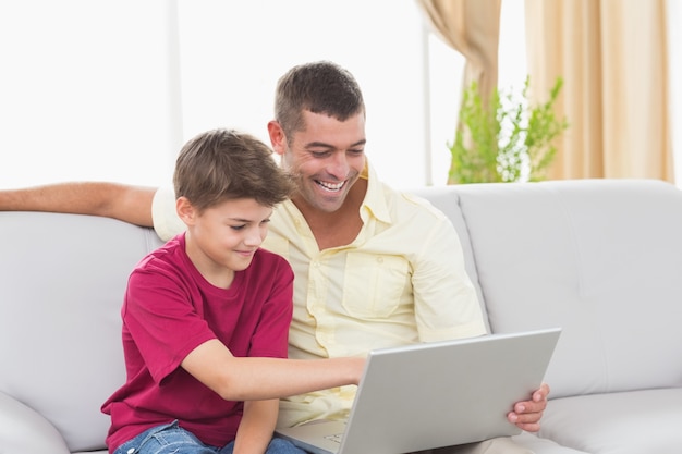 Father and son using laptop on sofa