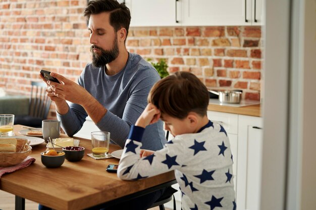 Photo father and son using smart phone sitting at table