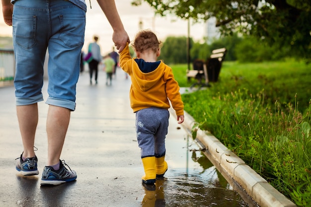 Father and son walking in the fresh air in rubber boots on the puddles after the rain on summer day.