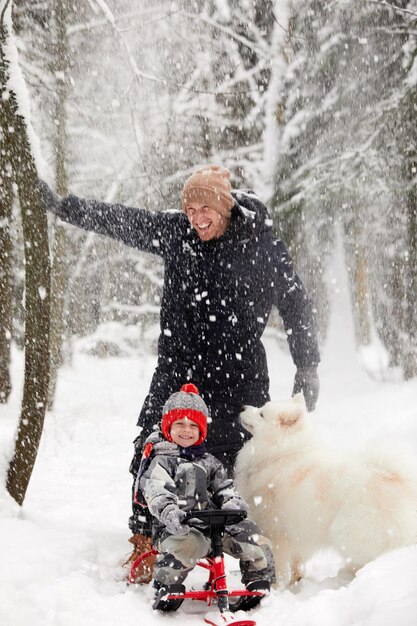 Father and son walking in snowy forest with his beagle dog in pine forest Family walking with pets and winter outfit concept image