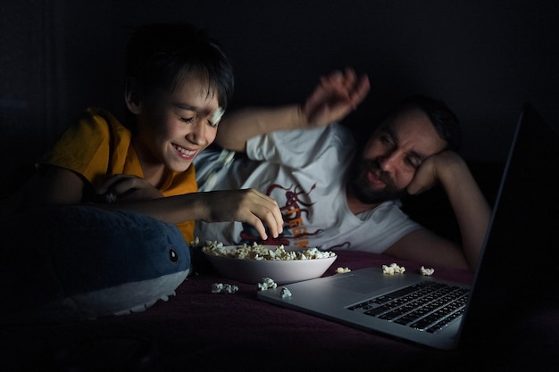 Photo father and son watching movie while eating popcorn at home
