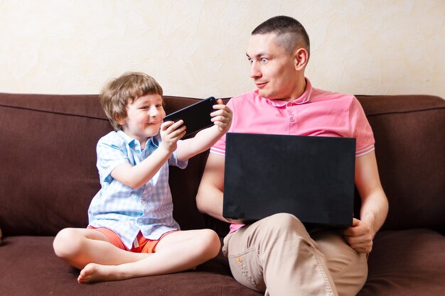 Father and son with laptop and mobile phone at home