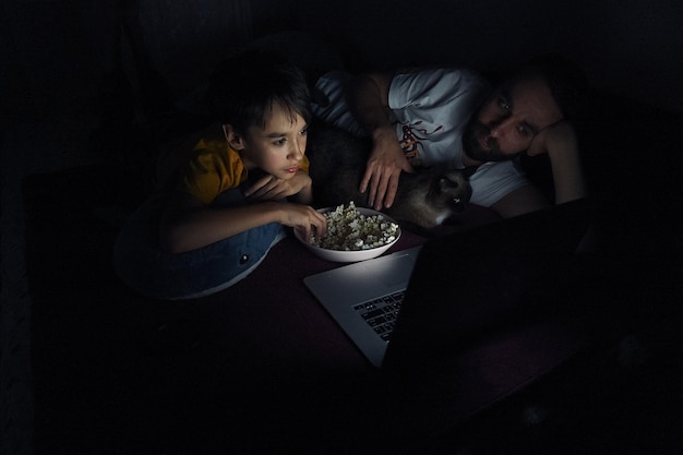 Photo father and son with popcorn looking at laptop