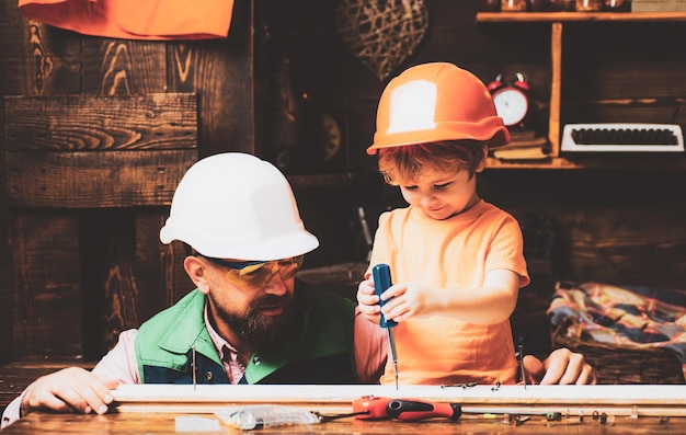 Father and sons are are building the furniture at home Little construction worker Father shows his little son how to use hammer and screwdriver Child growing