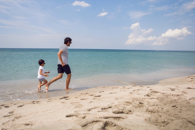 Father in a striped T-shirt walks with his son in shorts and a T-shirt walking on beach in summer during a vacation