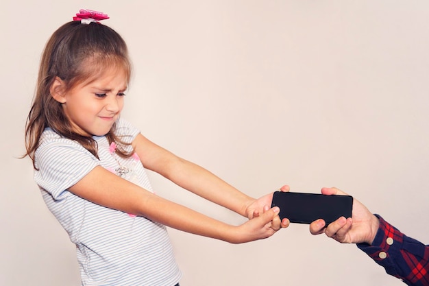 Photo father takes the phone from his daughter. children's addiction to mobile games. a thief stole a child's phone. angry dissatisfied girl snatches the phone from her parents hands