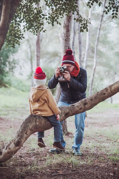 Father taking a picture of his son sitting on tree trunk in forest