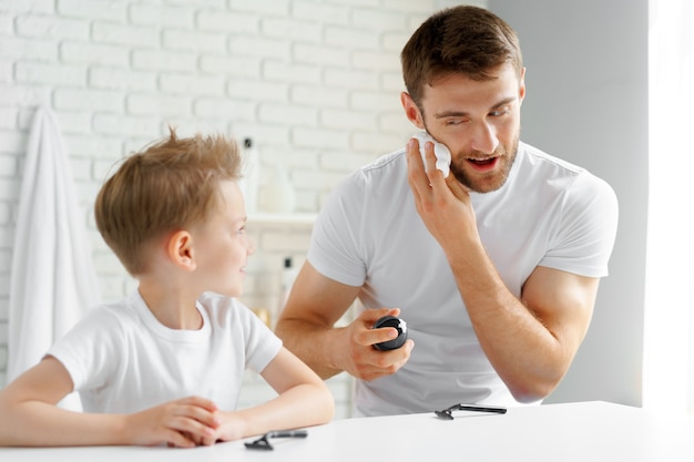 Father teaches his little son how to shave face in bathroom