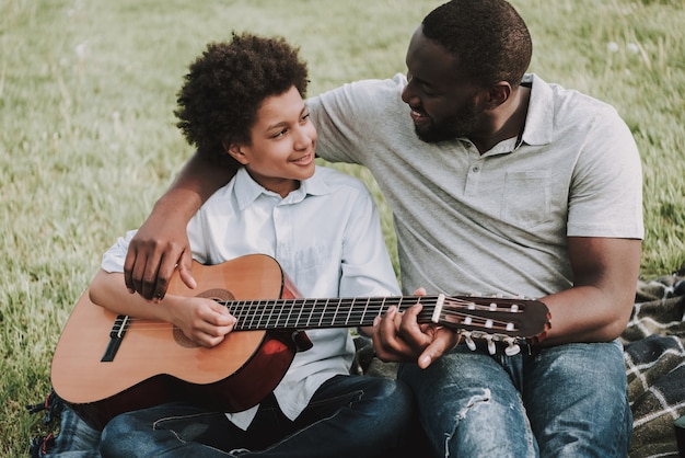 Father Teaches his Son to Play Guitar in Picnic.