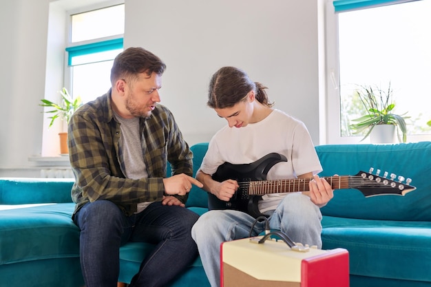 Father teaches his teenage son to play the electric guitar