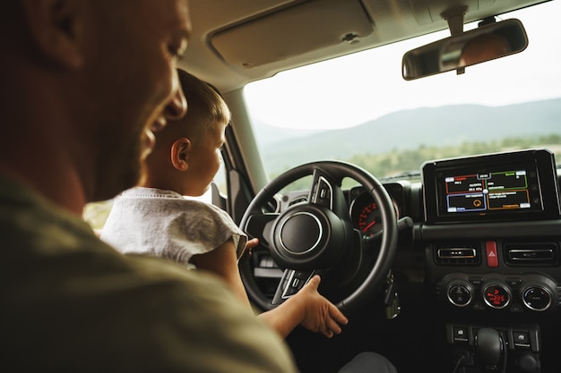 Father teaches little son to drive on road trip