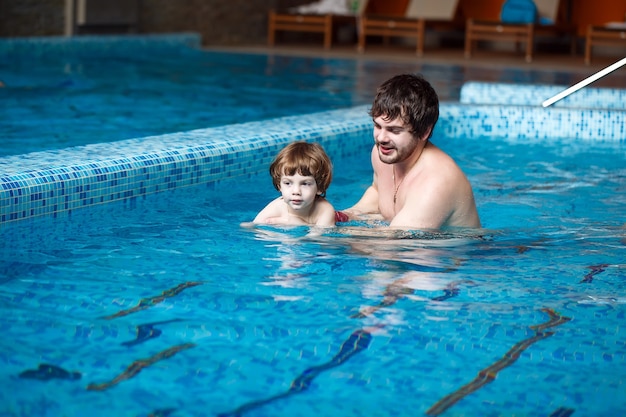 Father teaches son to swim in the pool.