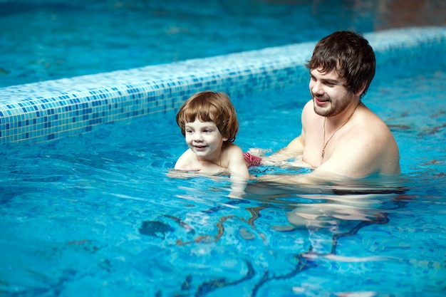 Father teaches son to swim in the pool.