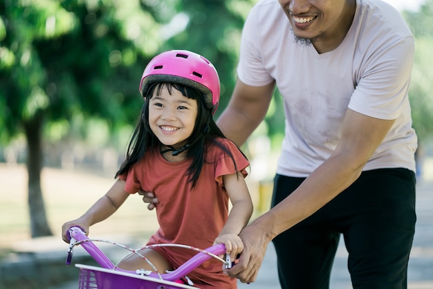 Отец учит дочь кататься на велосипеде в парке